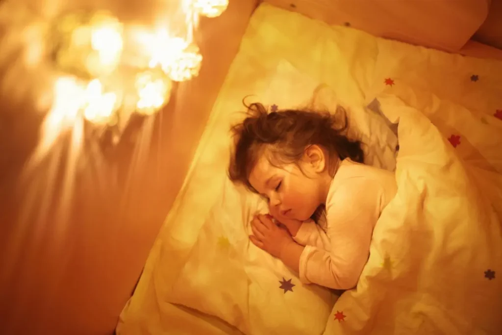 Toddler sleeping peacefully in bed at night with soft lighting and cozy blanket