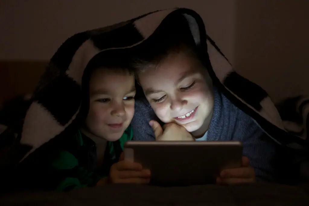 Tow kids using tablet in the blanket at night