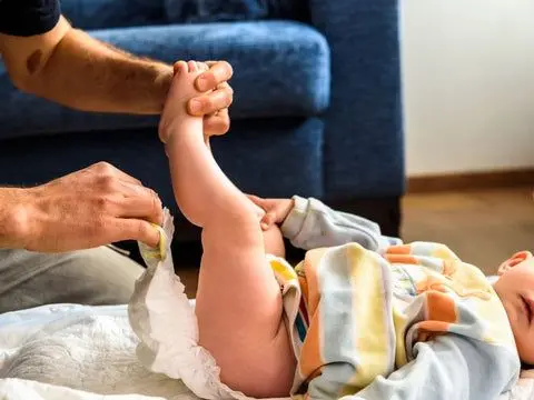 Adult changing baby's diaper on mat